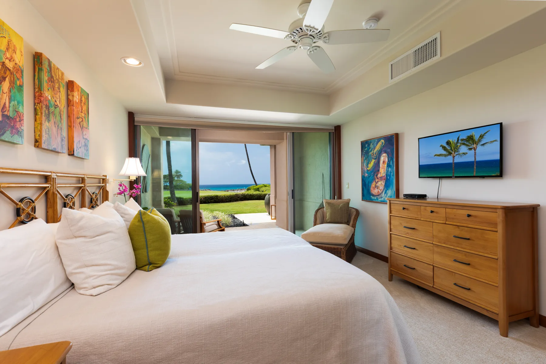 A bedroom with a bed, dresser, and sliding glass doors opening to an ocean view.