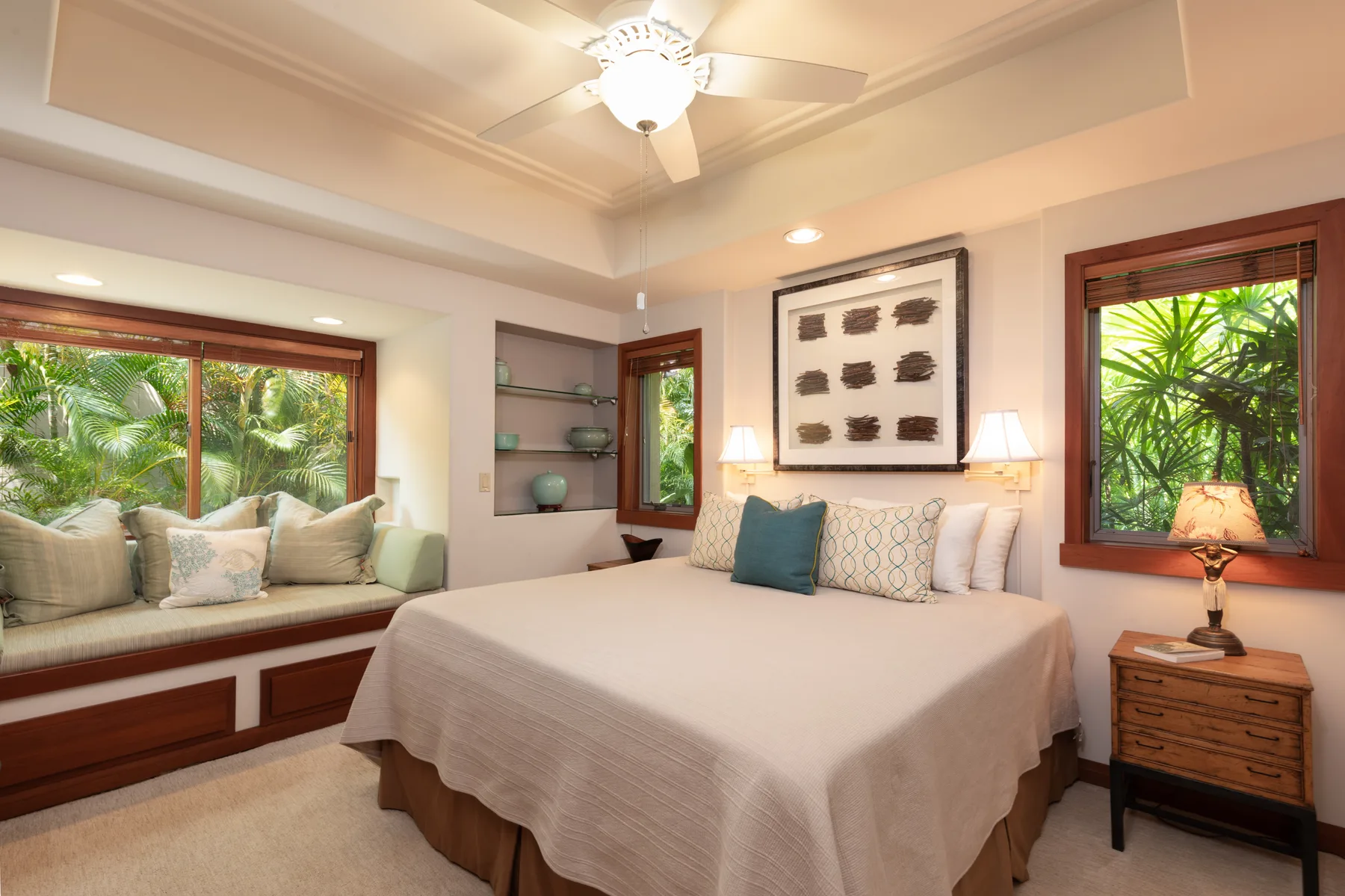 A bedroom with a bed, window seating, and leafy views outside.