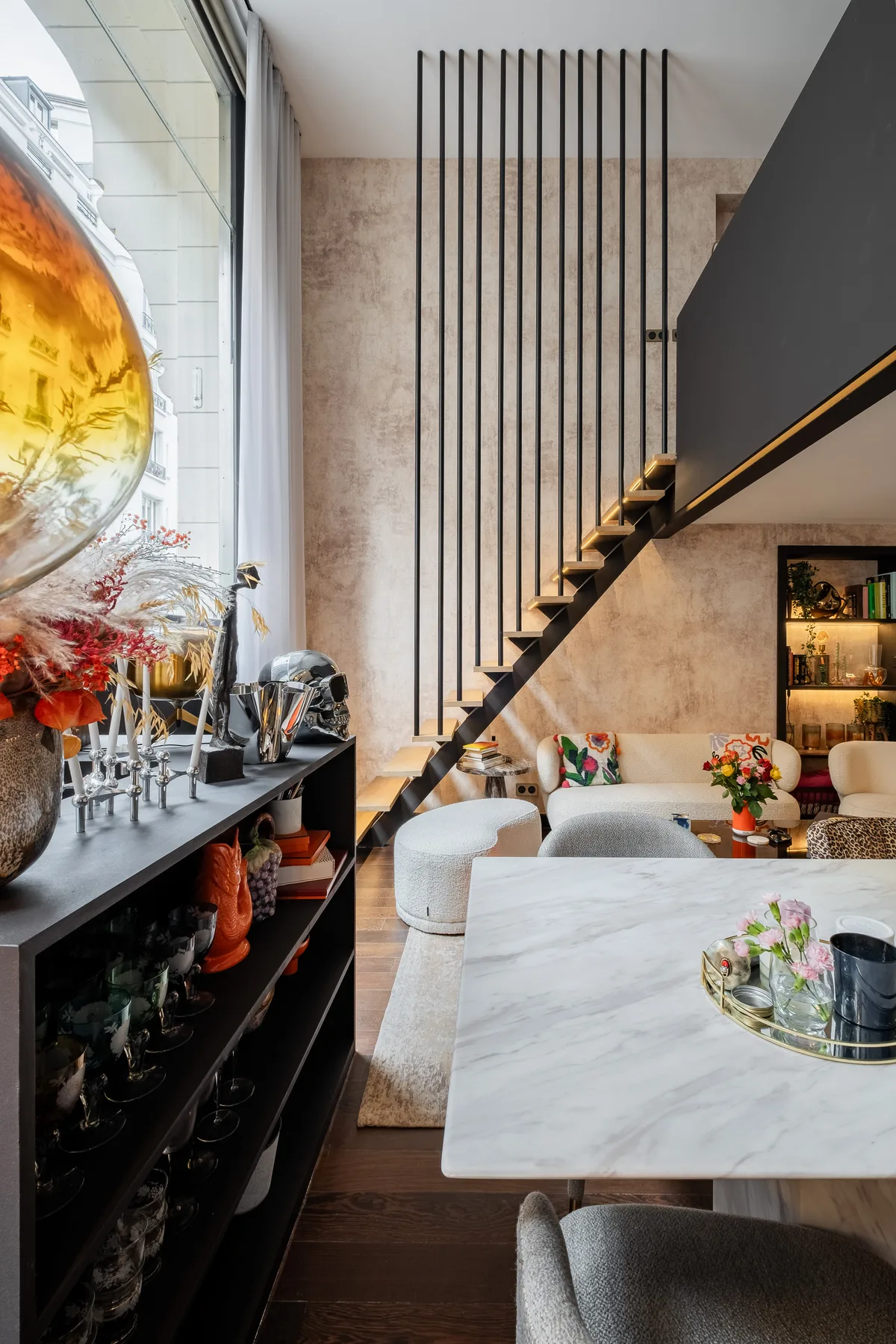 A modern living and dining area features a sculptural staircase and a marble dining table.