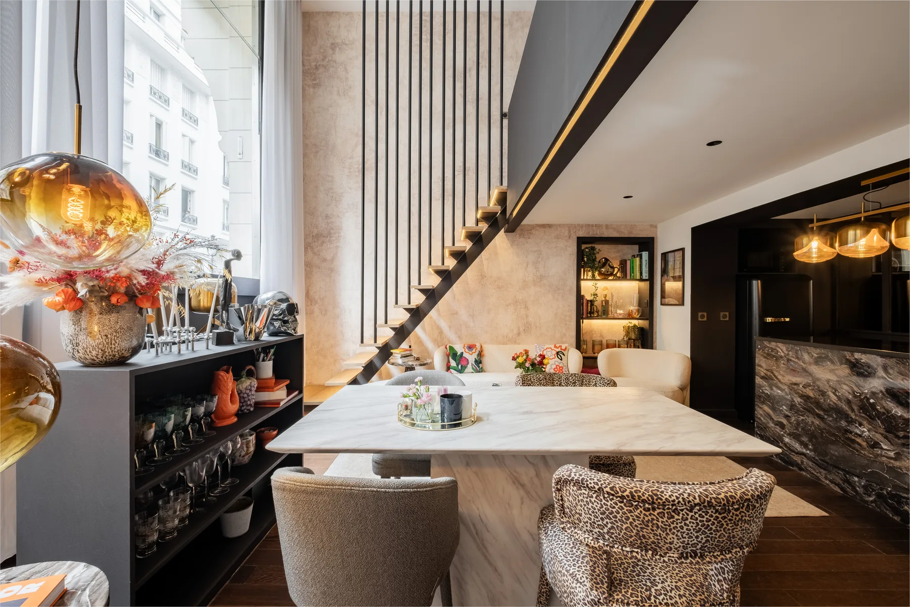 A modern dining area features a marble table beneath a staircase.