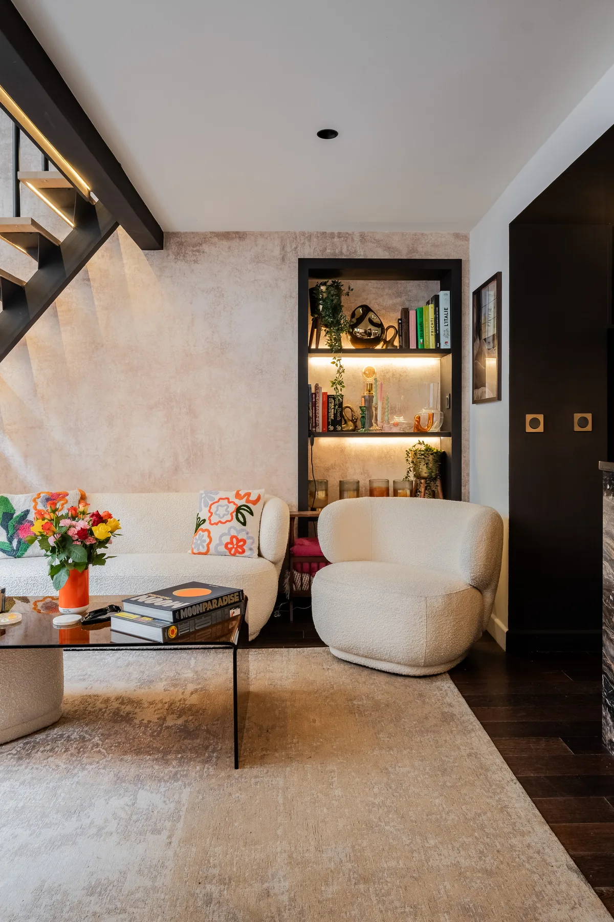A modern living room with upholstered seating, a coffee table, and illuminated shelves.