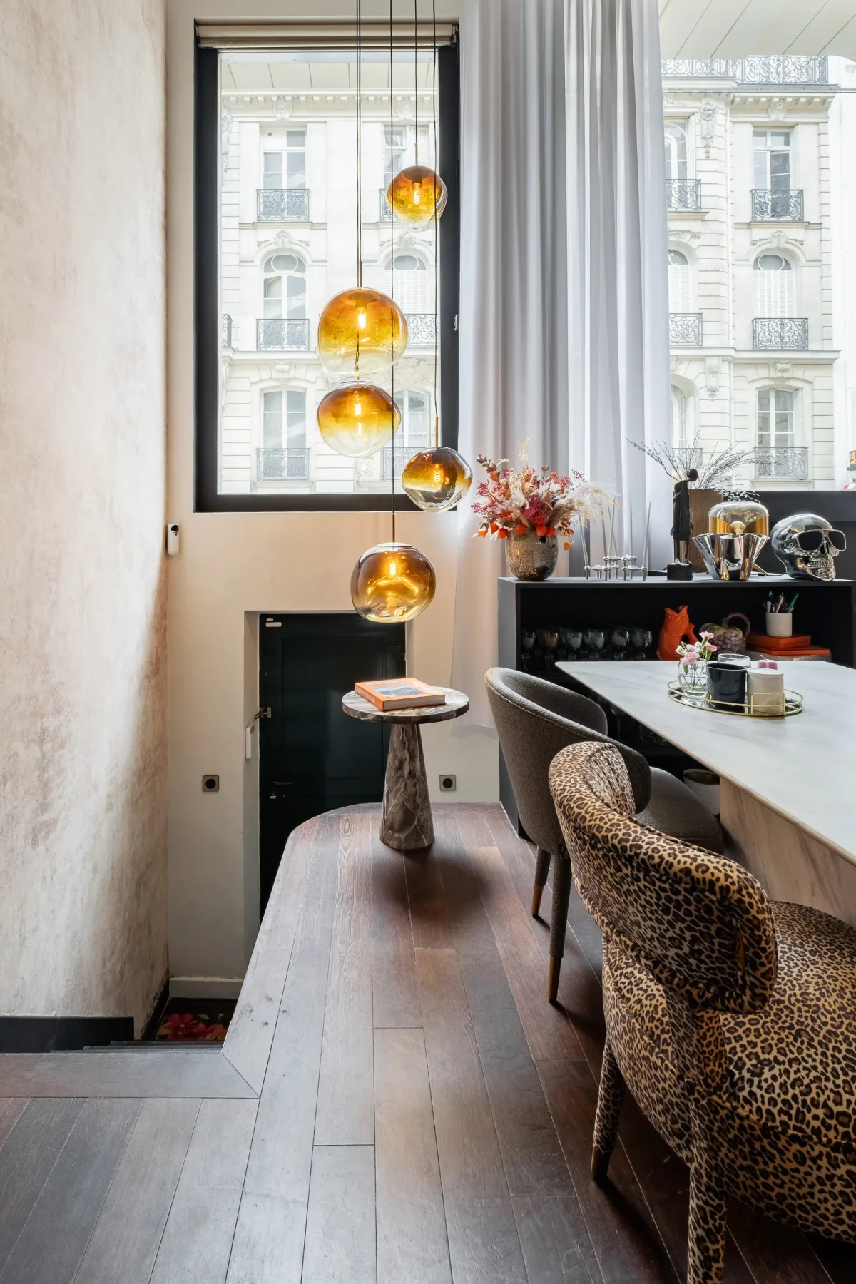 A dining area with a long table and pendant lights beside a large window.