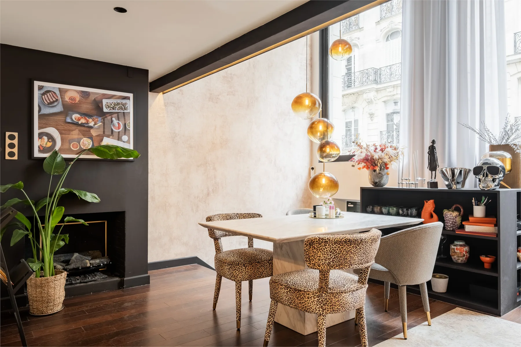 A dining area with a table and chairs beside large windows and a fireplace.