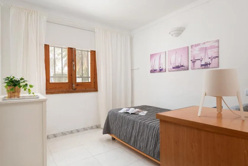 A bright bedroom with a bed, wooden desk, and window framed by white curtains.