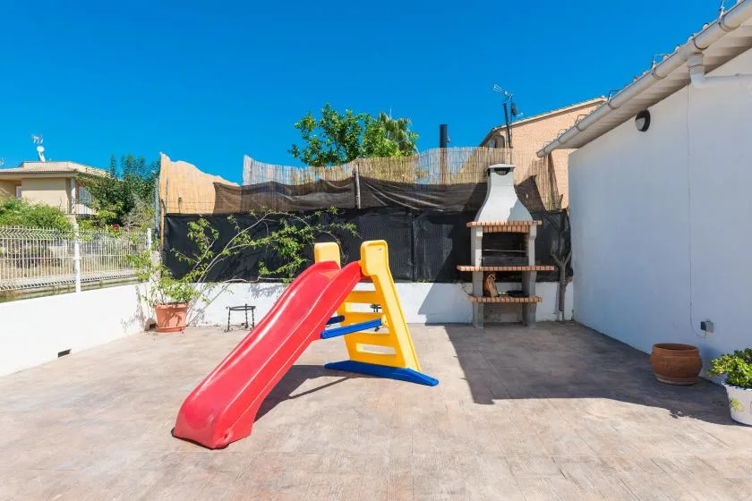 A sunny outdoor play area features a colorful slide beside a built-in barbecue.