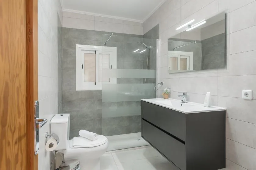 A tiled bathroom with a glass shower, toilet, and sink vanity.