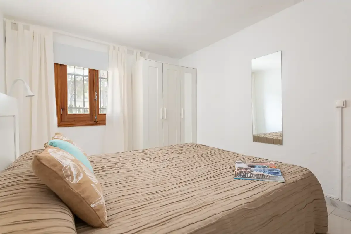 A bedroom with a neatly made bed and a window framed by curtains.