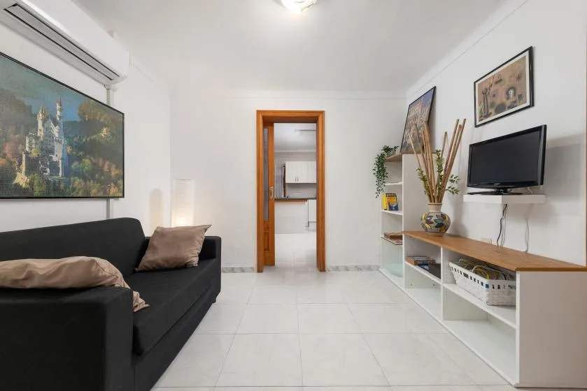 A bright living room with dark seating, wall art, and a television above a low cabinet.