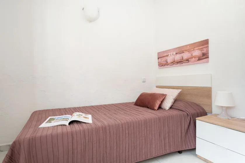 A bedroom with a bed covered in a mauve bedspread and an open book.