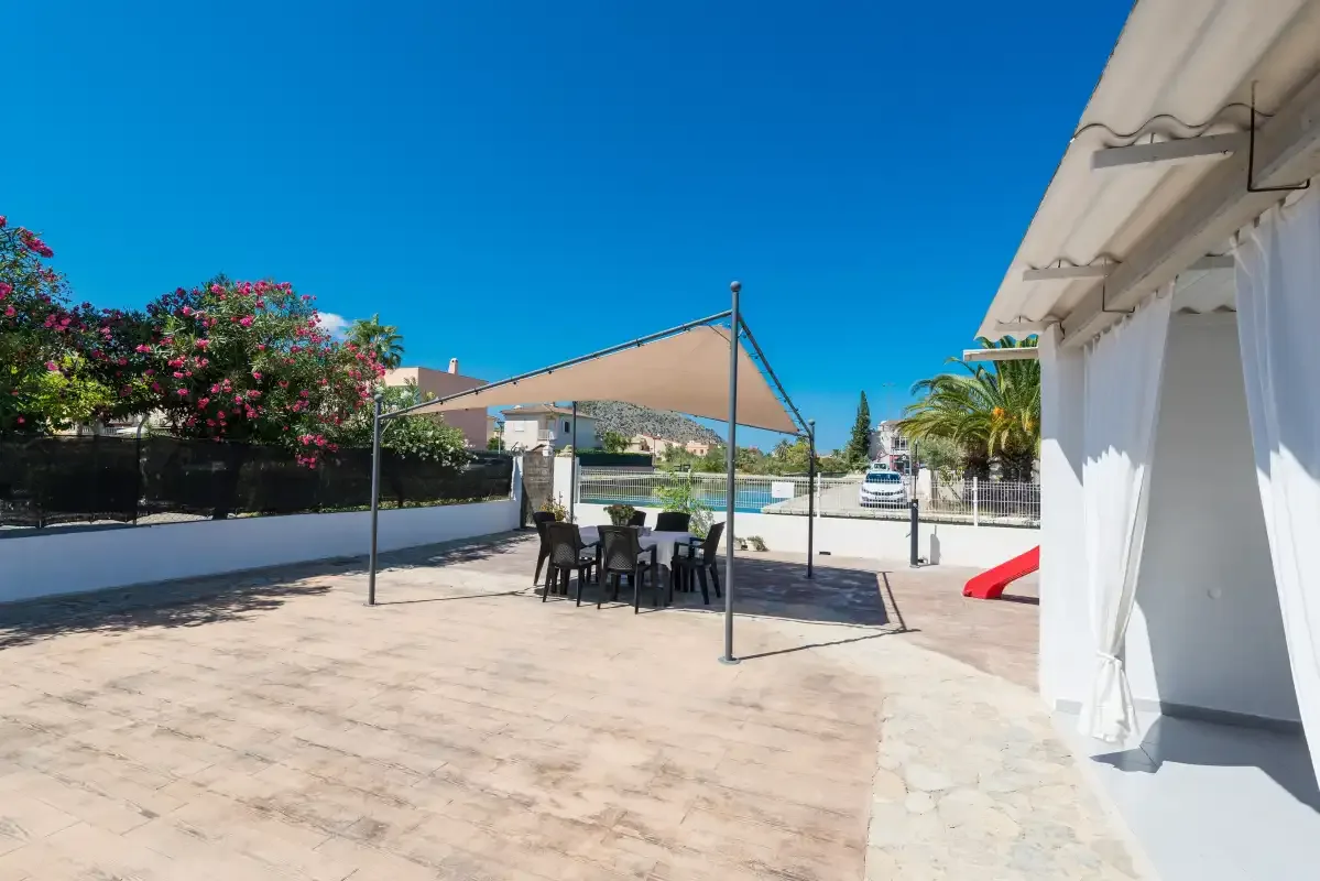 A paved outdoor patio with a shaded dining area and a red slide.