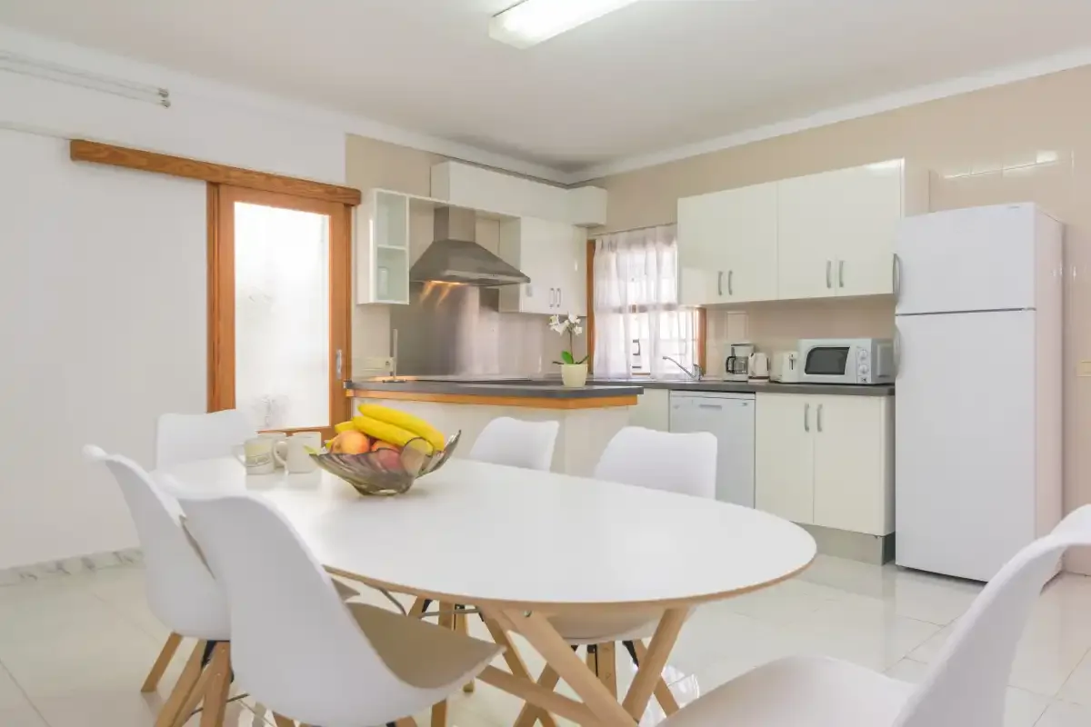 A dining area with a white table and chairs beside a kitchen.