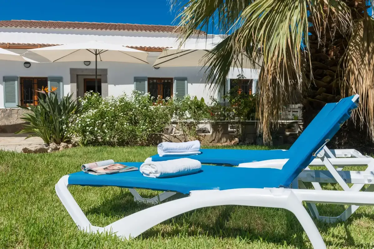 A blue sun lounger sits on the lawn in front of a white building.
