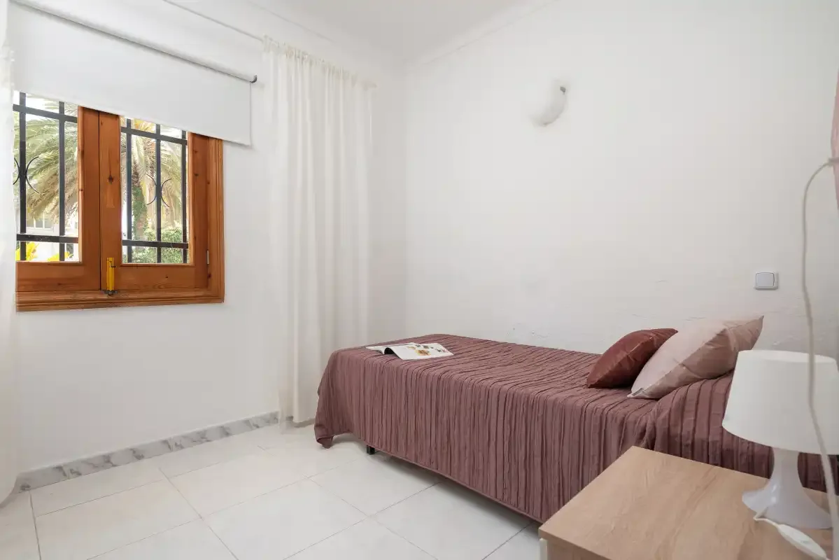 A bright bedroom with a bed beside a wood-framed window.