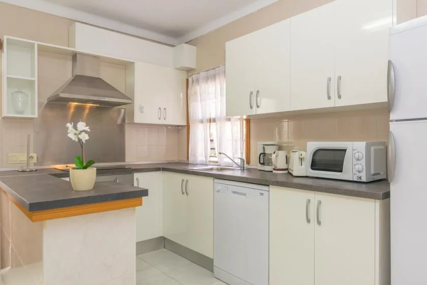 A bright kitchen with white cabinets, dark countertops, and a microwave.