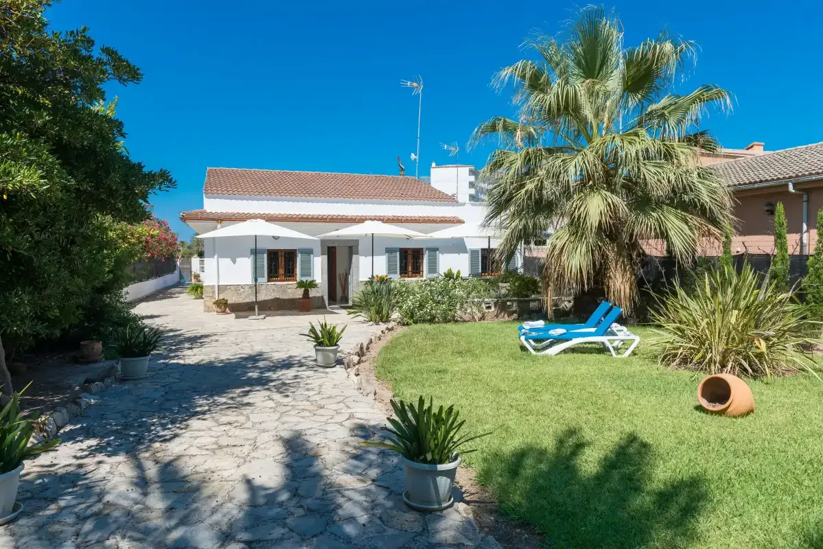 A house opens onto a paved garden with lawn and palm trees.