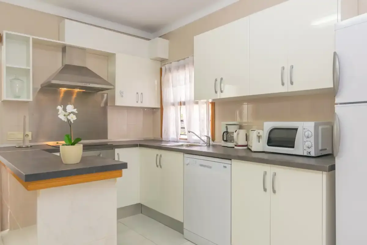A bright kitchen with white cabinets, dark countertops, and a microwave.