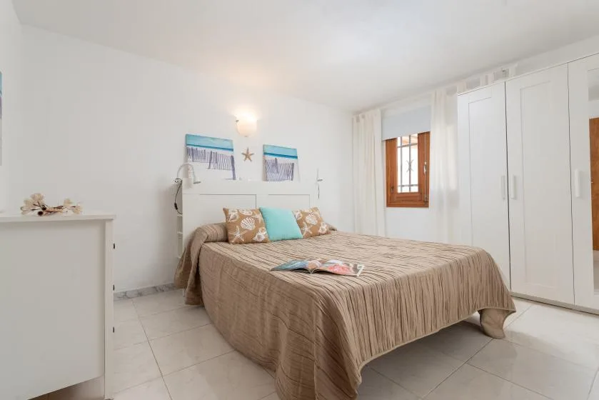 A bright bedroom with a bed, white wardrobes, and a small window.