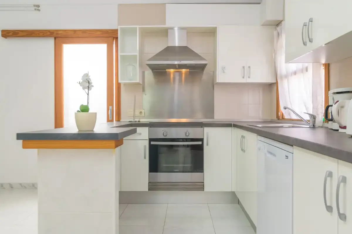 A bright kitchen with white cabinets, a central oven, and a dark countertop.
