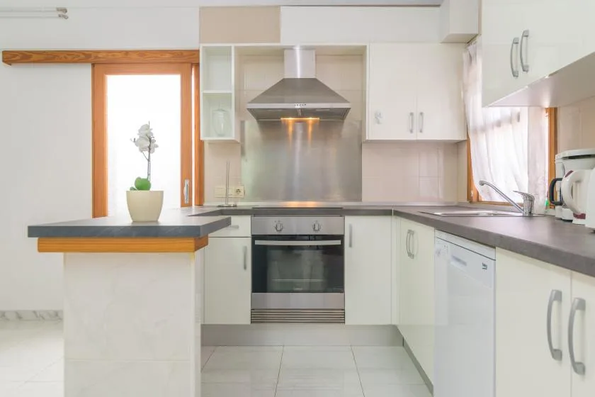 A bright kitchen with white cabinets, a central oven, and dark countertops.