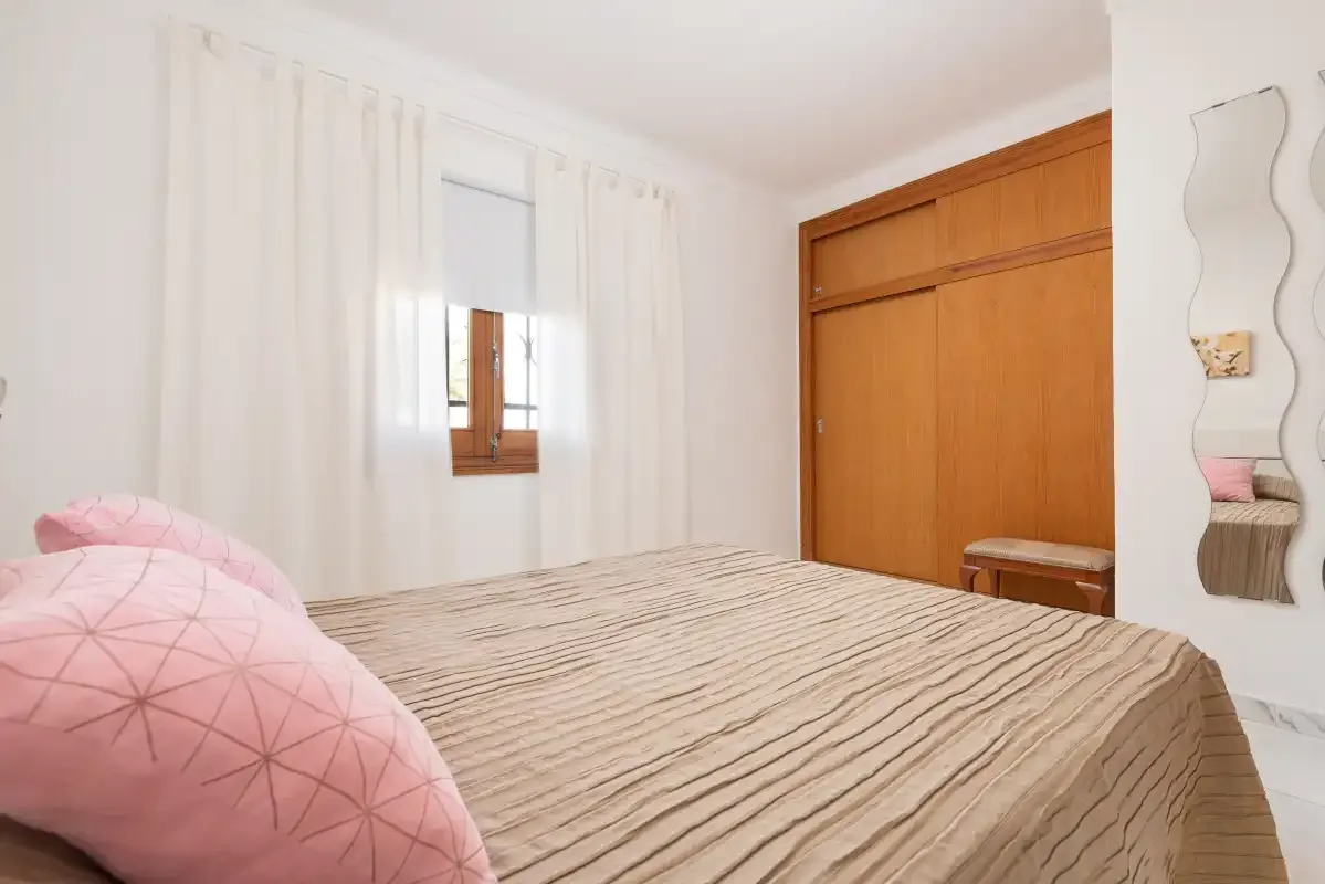A bedroom with a bed, pink pillows, and a wooden wardrobe.