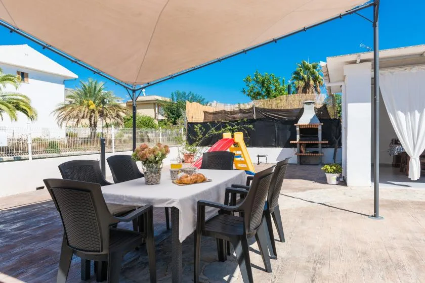 A shaded outdoor dining area with table seating beside a barbecue grill.