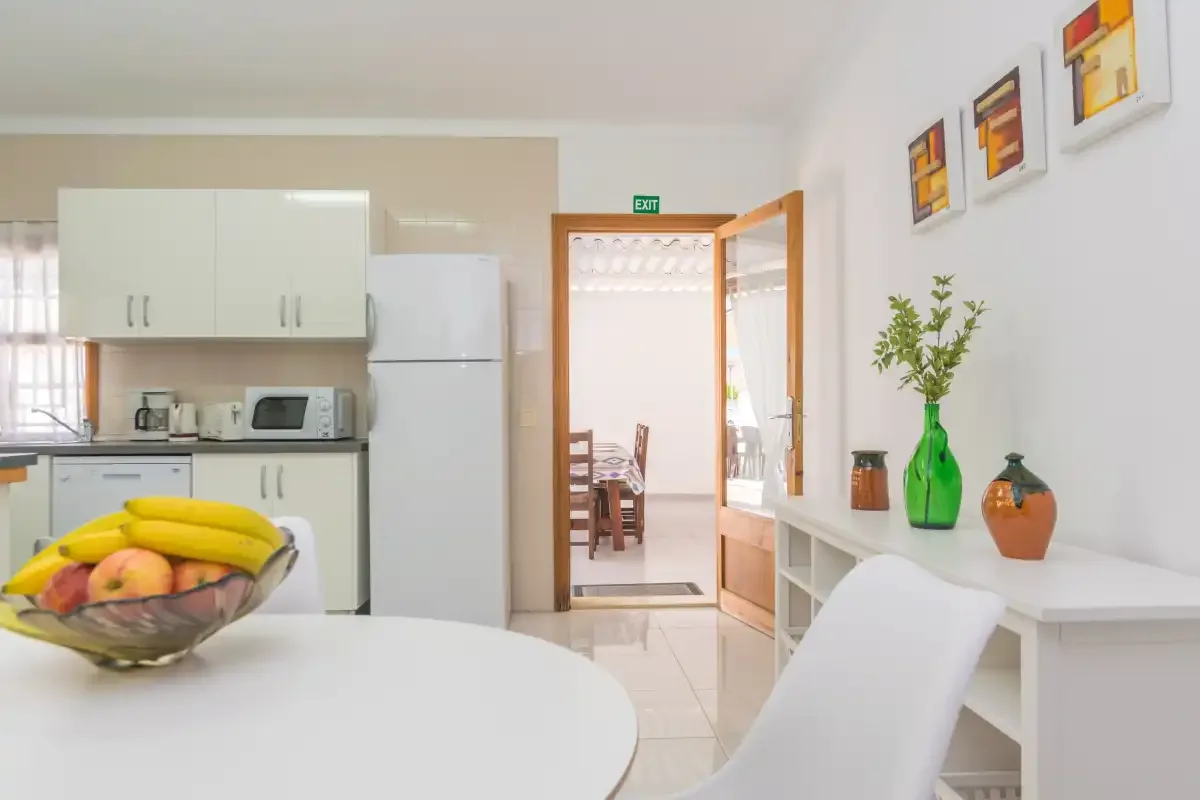 A bright kitchen and dining area with a fruit bowl on the table and an open doorway.