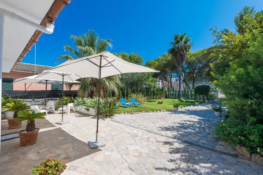 Un patio soleado con una sombrilla grande, asientos al aire libre y vegetación alrededor.