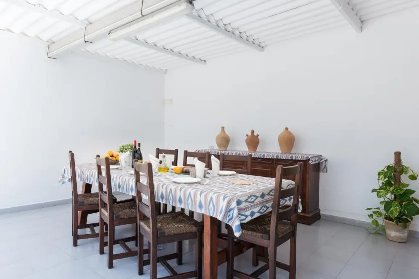 A dining room with a long table covered by a patterned cloth and wooden seating.