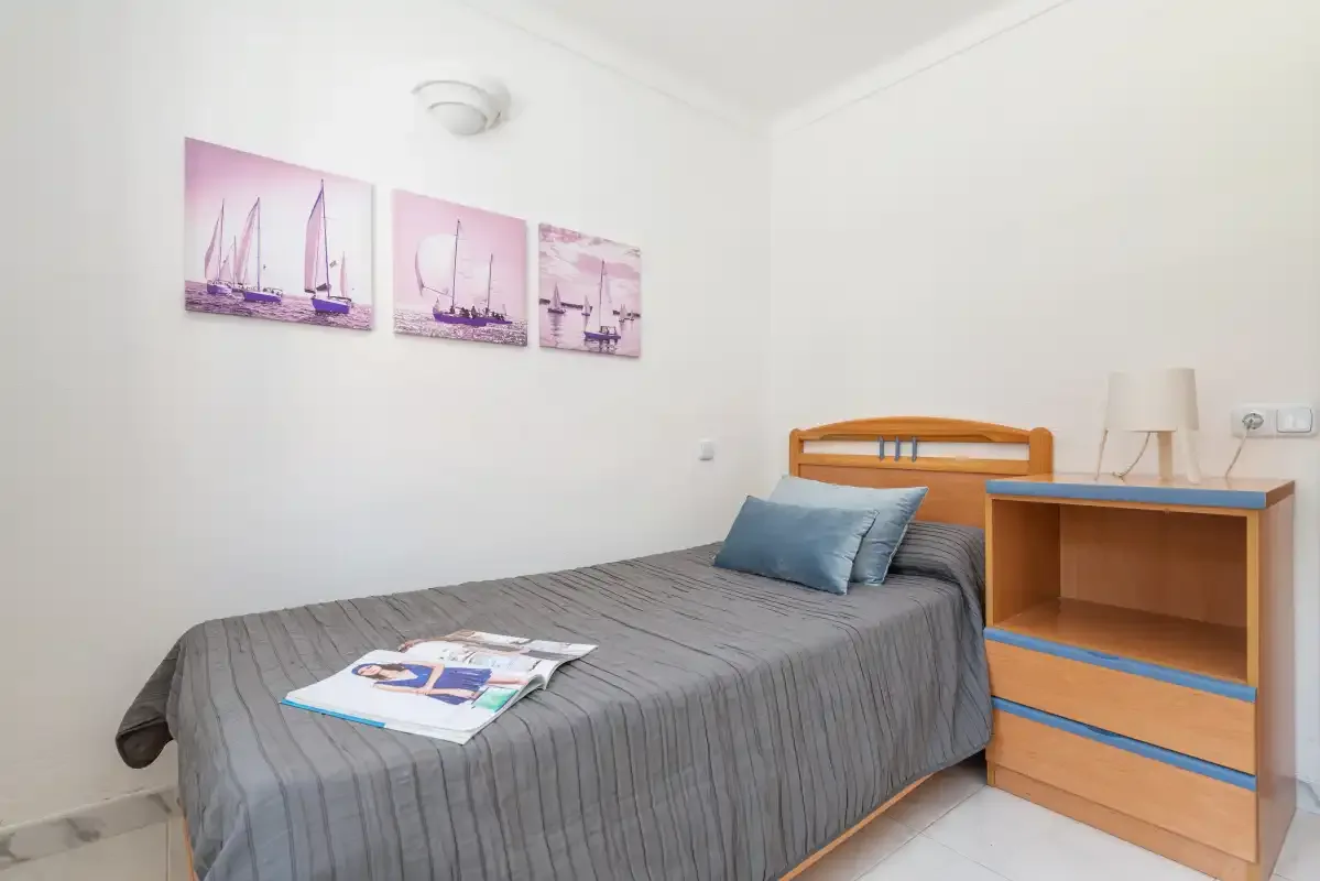 A bedroom with a single bed, blue pillows, and a wooden bedside cabinet.