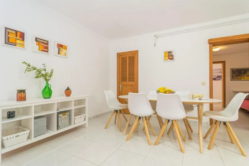 A bright dining area with a table, white seating, and a low display shelf.