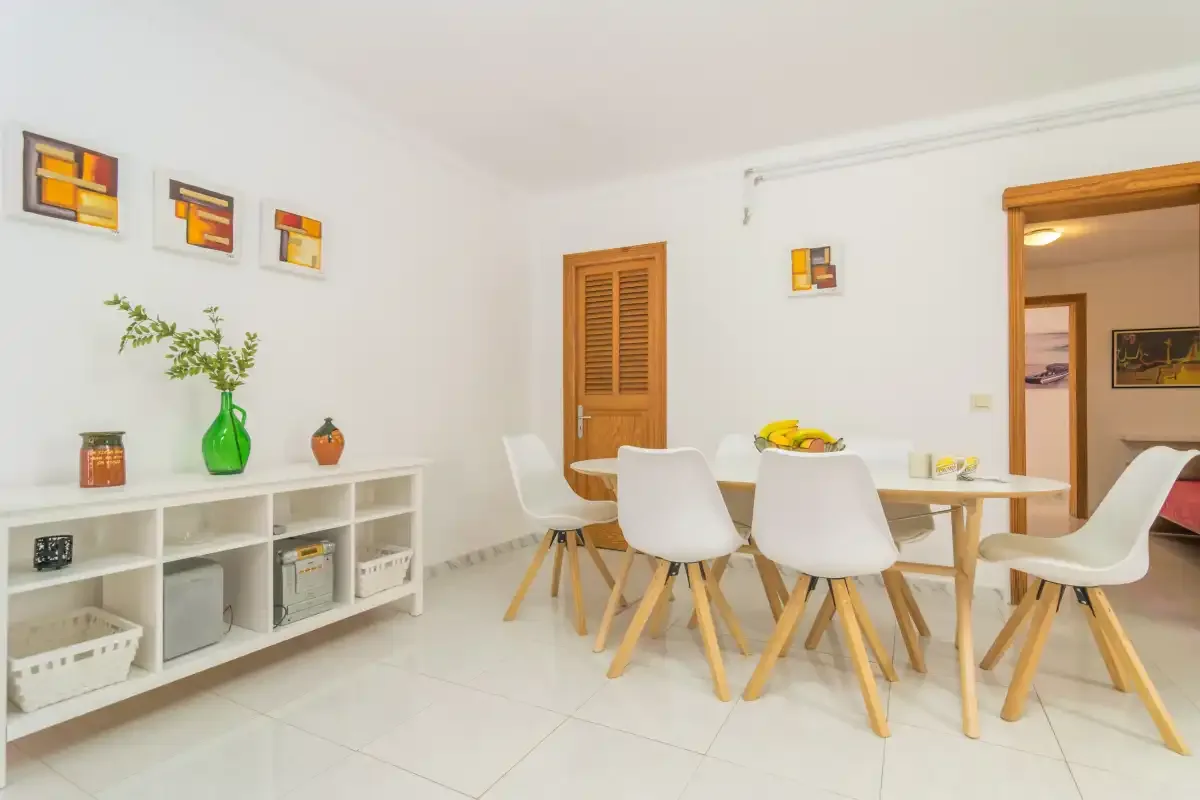 A bright dining area has a table, white seating, and a low open shelving unit.