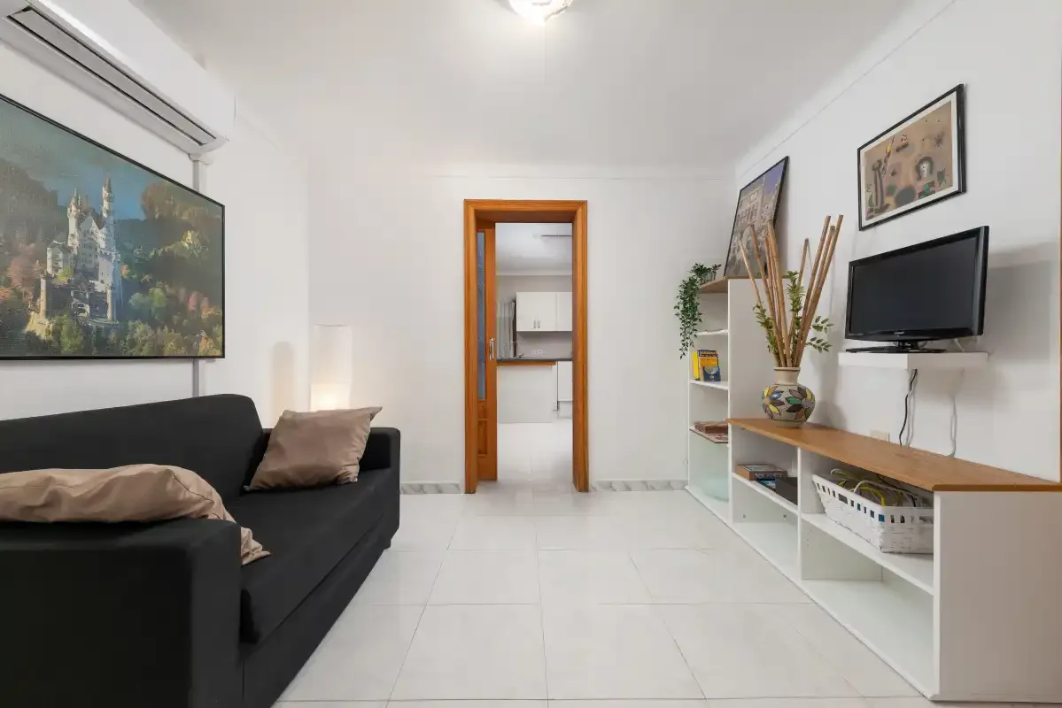 A living room with a black sofa, television, and an open doorway.