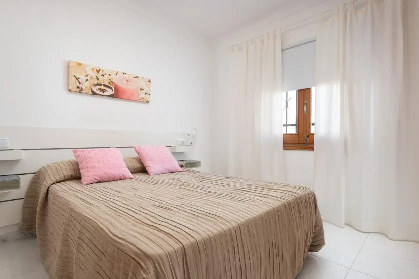 A bedroom with a bed dressed in beige bedding and a small window.