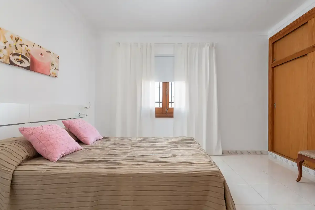 A bright bedroom with a bed beneath a curtained window.
