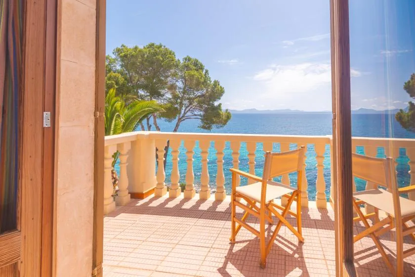 A wooden chair sits on a sunlit balcony overlooking the sea.