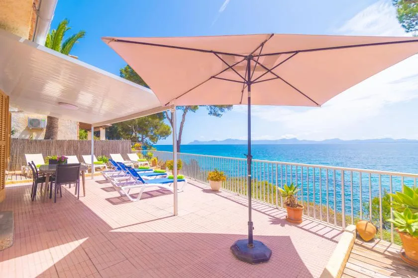 A seaside patio with lounge seating, an open umbrella, and a view across the water.