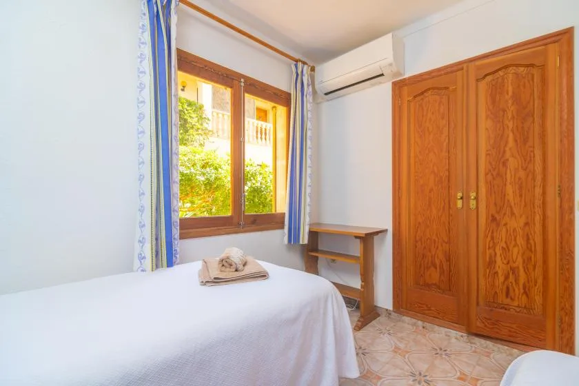 A bedroom with a bed beside a window and wooden wardrobe.