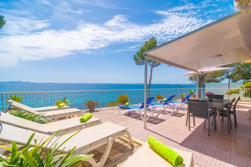 Una terraza junto al mar con asientos, comedor y vistas al agua azul.