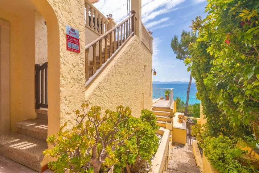 A sunny stone walkway and staircase lead toward a terrace overlooking the sea.