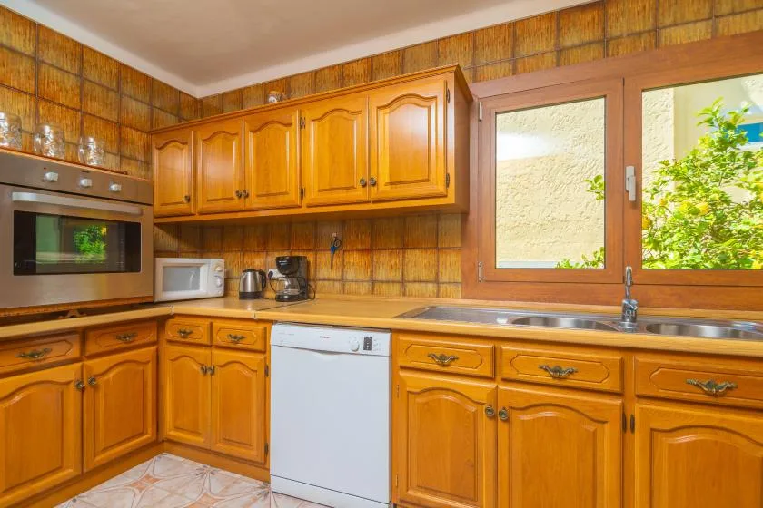 A kitchen with wooden cabinets, a sink, and a dishwasher beneath the window.