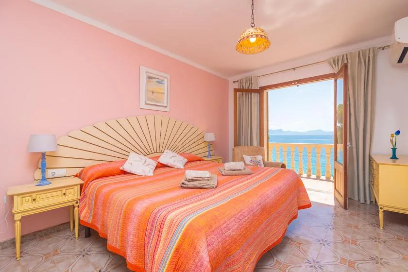 A bedroom with a large bed facing an open balcony overlooking the sea.