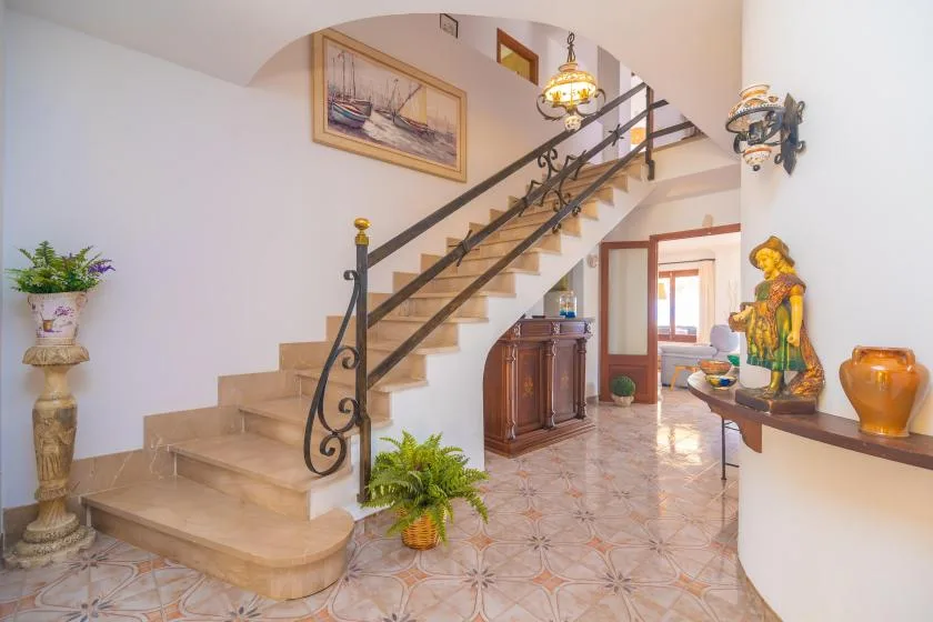 An interior hallway with a staircase, patterned tile flooring, and decorative furnishings.