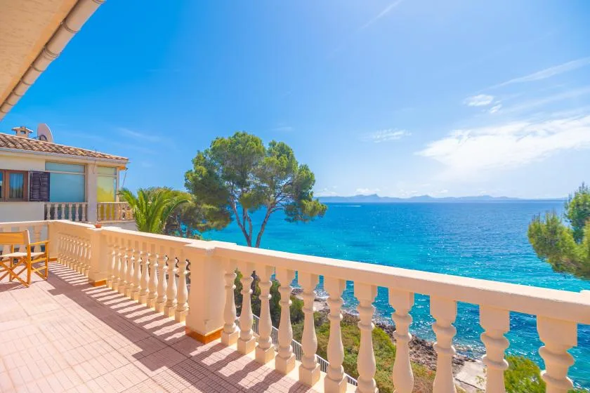 A sunlit seaside terrace overlooks the blue water and distant coastline.