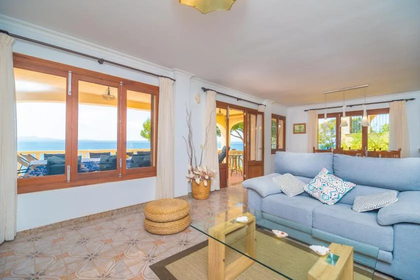 A bright living room with pale blue seating and large windows overlooking the sea.