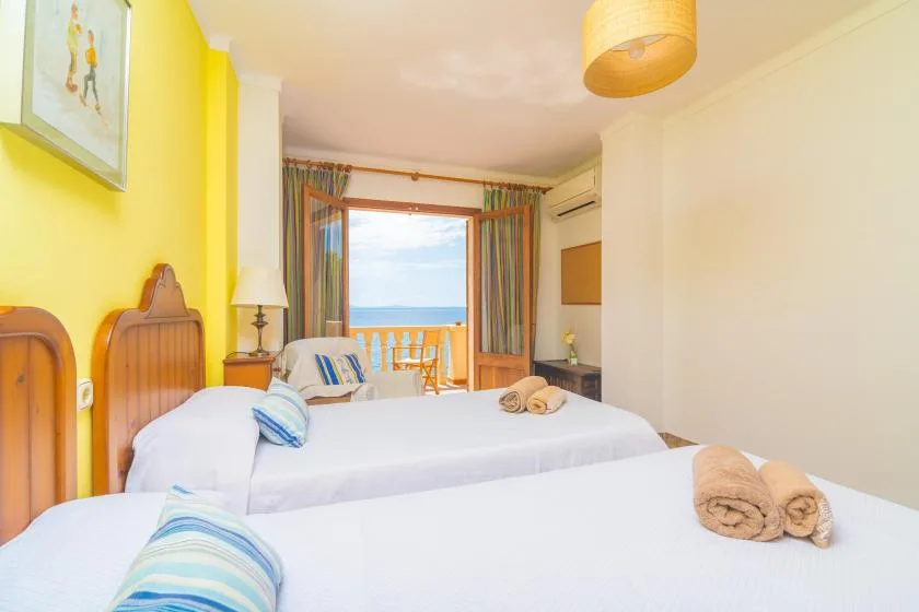 A bright bedroom with two beds and a balcony overlooking the sea.