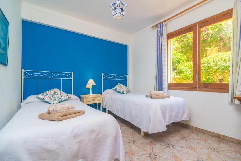 A bright bedroom with two beds beside a large window.