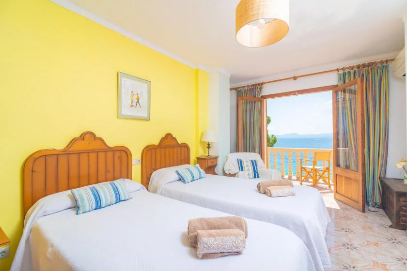 A bright bedroom with two beds and an open balcony doorway.