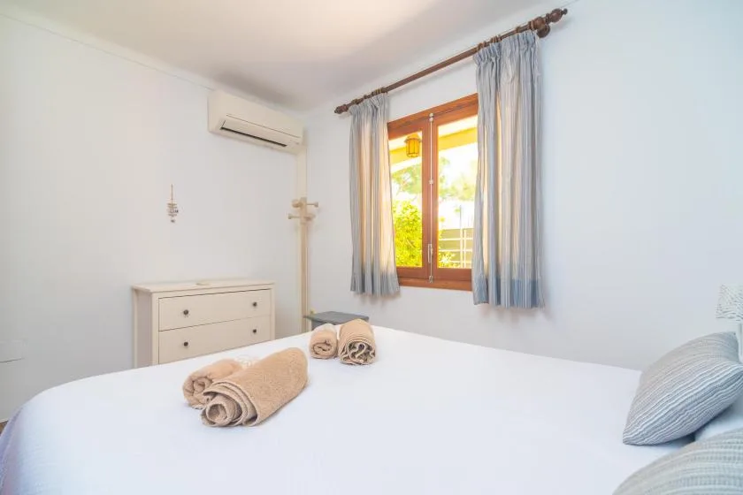 A bright bedroom with a neatly made bed and a sunlit window.
