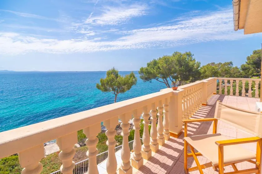 A sunlit seaside terrace overlooks the blue water and nearby trees.