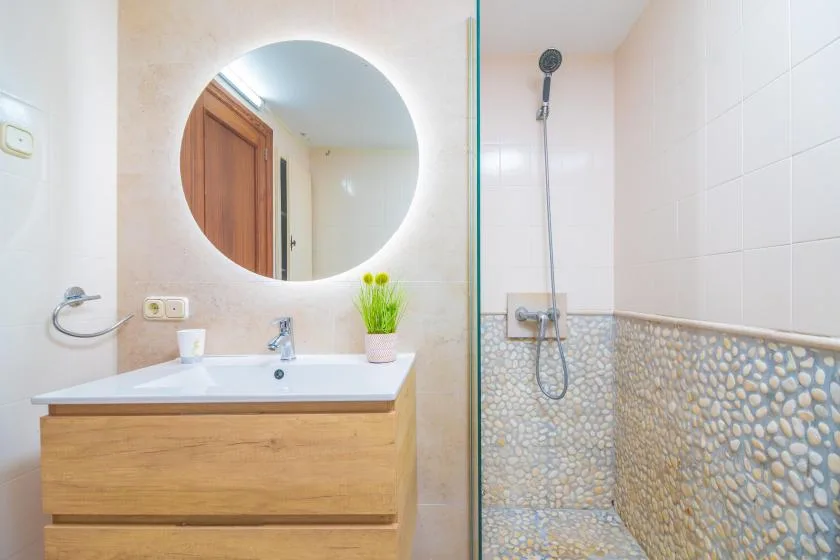 A bathroom with a sink, round mirror, and glass shower screen.